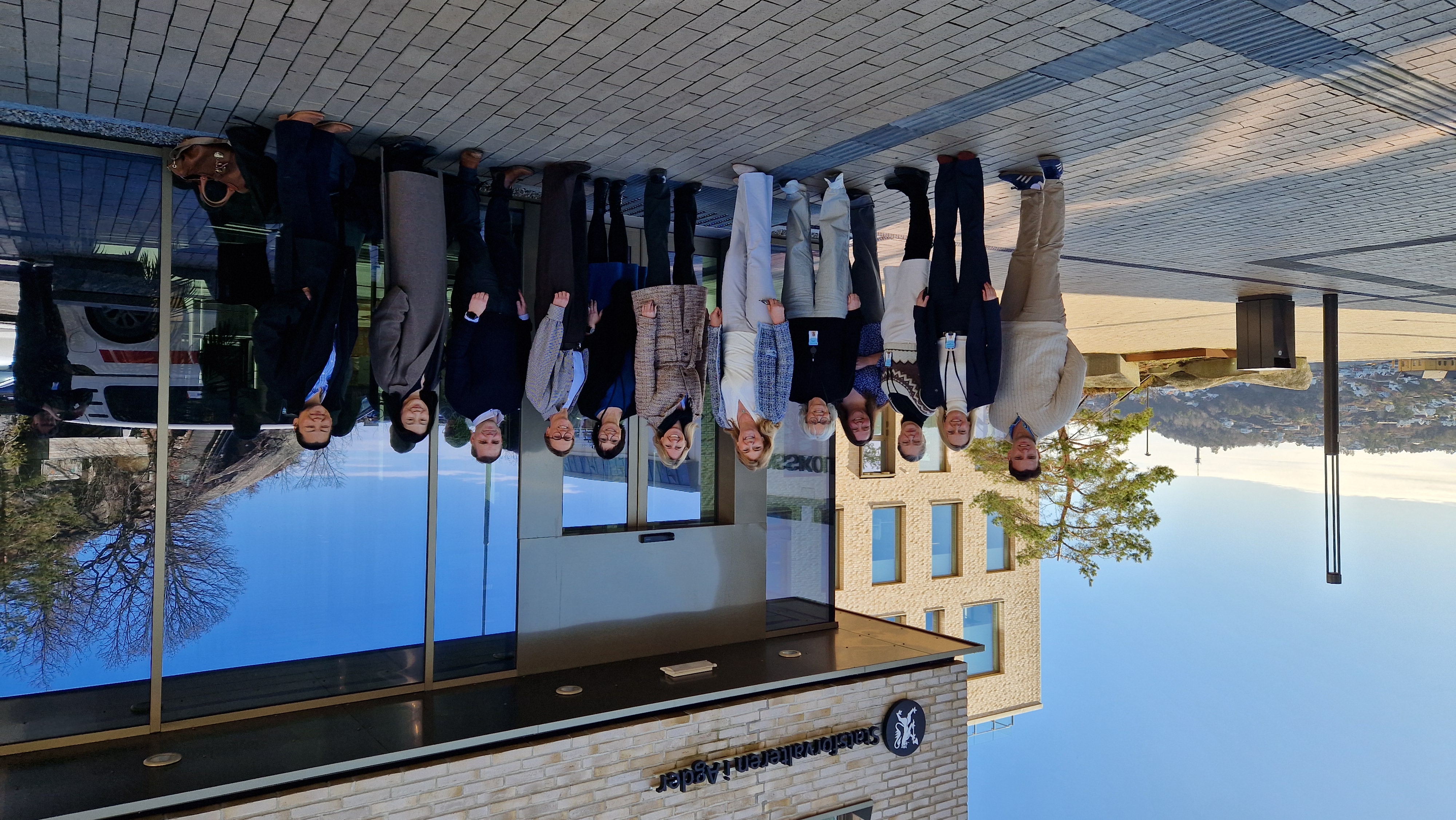 En gruppe smilende mennesker står på rekke fremfor bygg med logoen "Statsforvalteren i Agder"