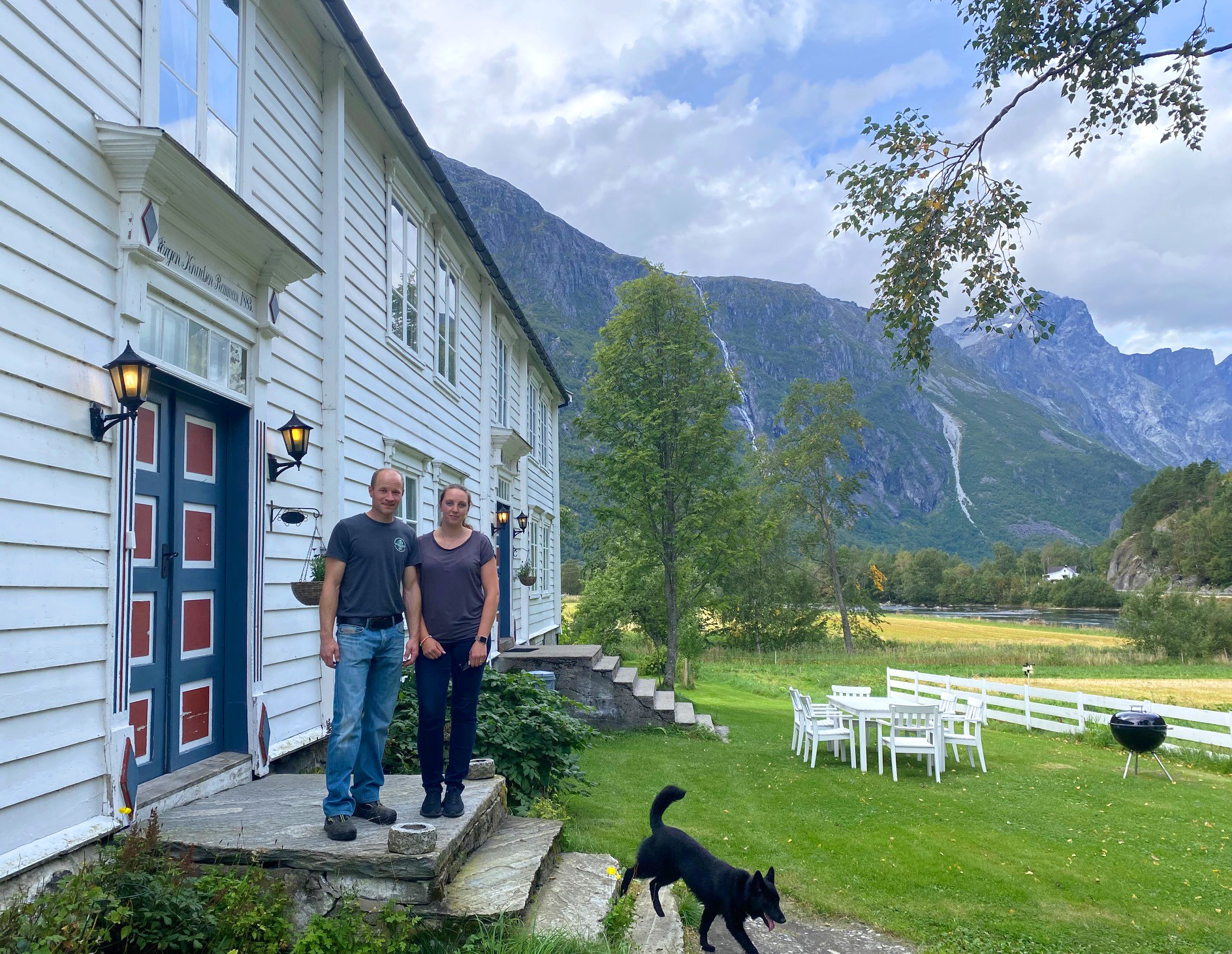 Marius Remmem og Linn Kristin Hestad får Kulturlandskapsprisen 2025. Garden Remmem ligg ved Raumaelva i Romsdalen. Foto: Statsforvaltaren i Møre og Romsdal, Marie Teigland Marius Remmem og Linn Kristin Hestad står på trappa framfor eit kvitt våningshus. En svart hund går ned trappa. Fjell i bakgrunnen og grønt gras ved huset.