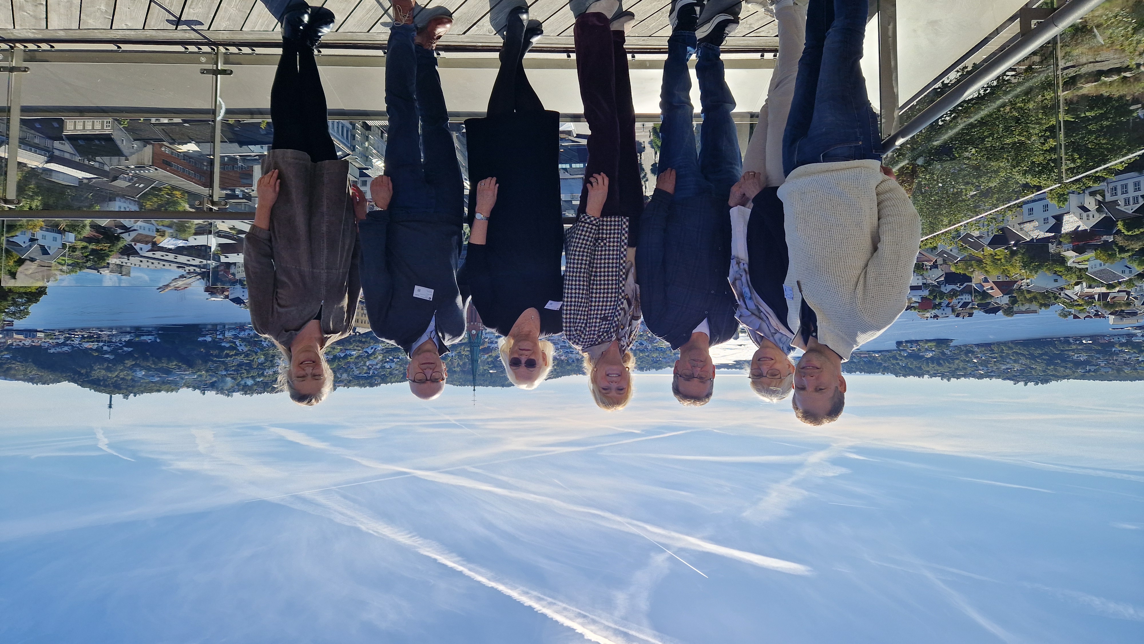 Syv mennesker står på linje på en terrasse med Arendal by i bakgrunnen