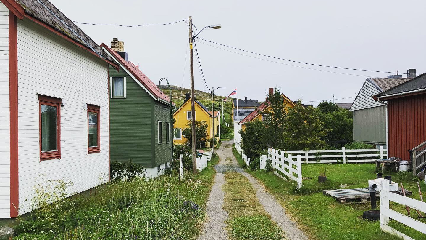 Bugøynes er et av flere mindre tettsteder i Sør-Varanger kommune med lang avstand til kommunesenteret Kirkenes. Foto: Emil Harjo Indsetviken / Statsforvalteren i Nordland. Rett grusvei med hus på begge sider.