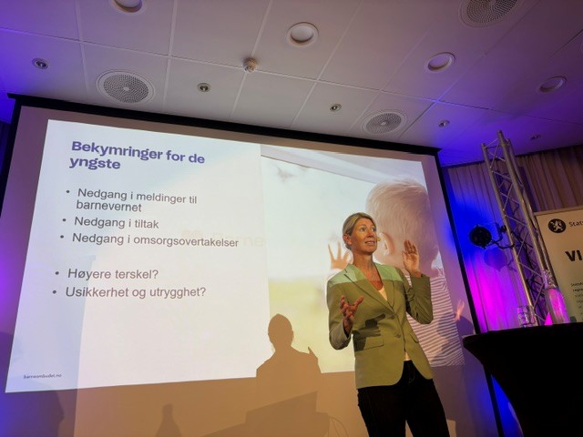 Person holder foredrag på en konferansescene foran et lysbilde om bekymringer knyttet til nedgang i meldinger, tiltak og omsorgsovertakelser i barnevernet.