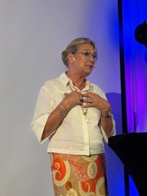 Statsforvalter Gina Lund står på en scene og holder innlegg under et seminar. Bildet er tatt foran en presentasjonsskjerm og scenebelysning i blå og lilla toner. Lund innleder seminaret om forebygging av vold og overgrep mot barn og unge under Arendalsuka.
