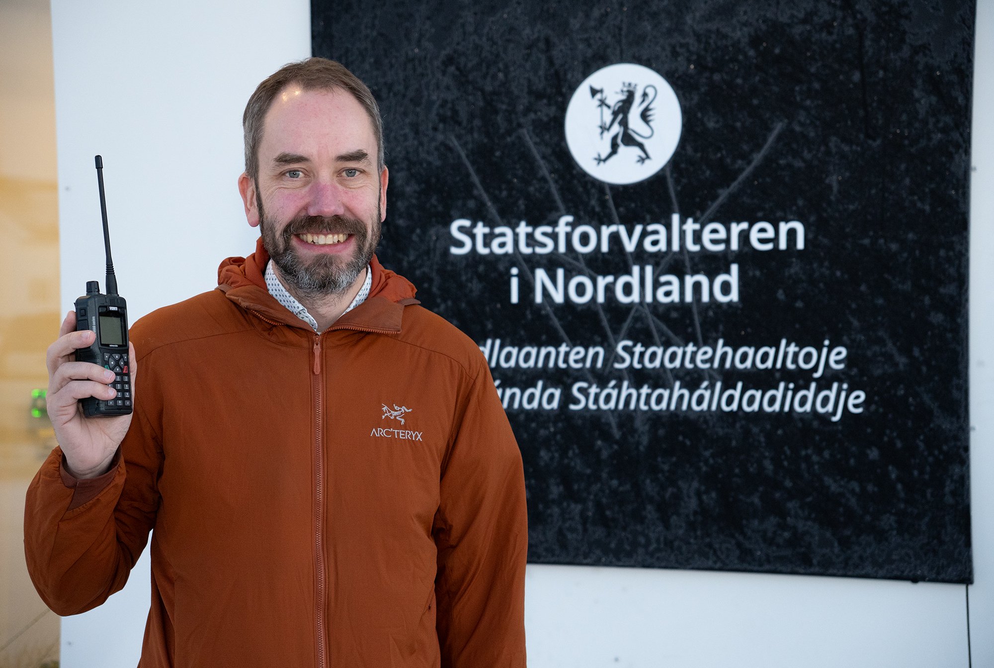 En mann med oransje jakke holder en telefon med antenne.