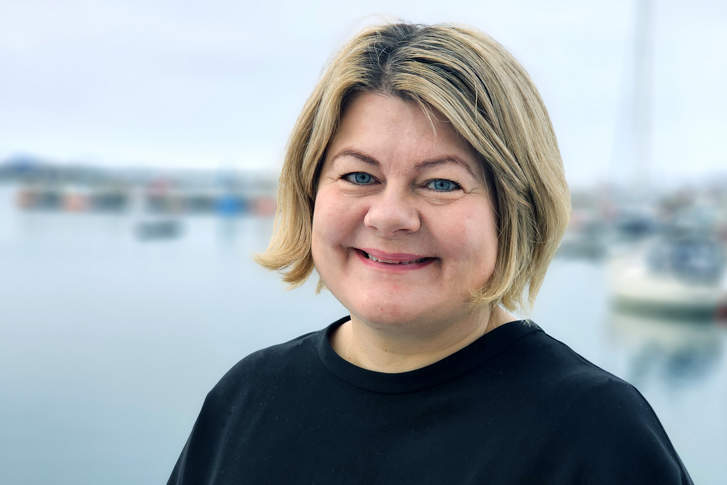 Silje Jakola-Fjeld - ny justis- og kommunaldirektør Foto: Sykehusinnkjøp HF. Silje Jakola-Fjeld - ny direktør hos Statsforvalteren i Troms og Finnmark. Smilende kvinne med lyst hår og sort genser. Vann/havn i bakgrunnen.