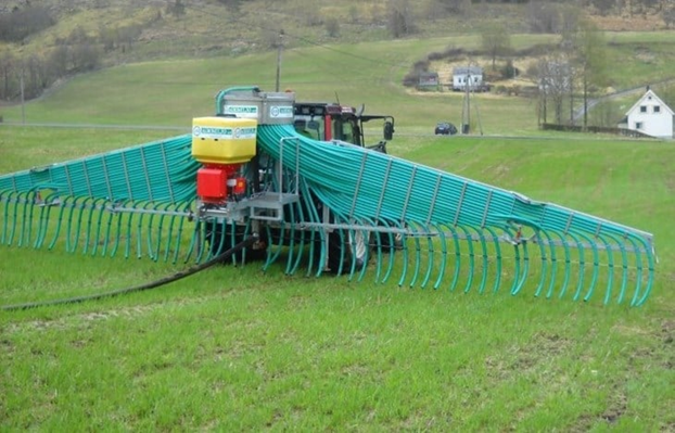 Traktor med gjødselspreiar på ei mark.