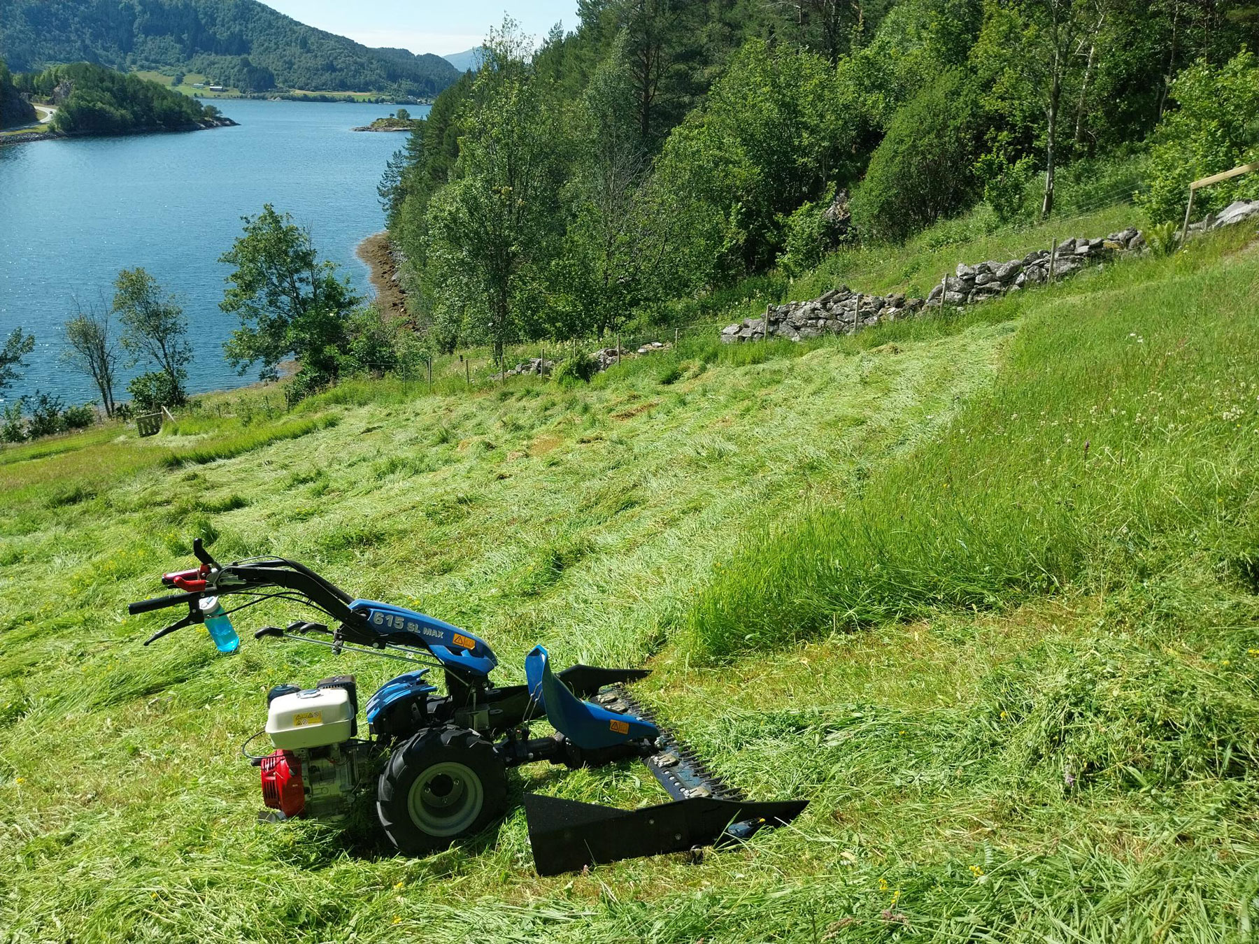 Lita slåmaskin i ein bratt grasbakke.
