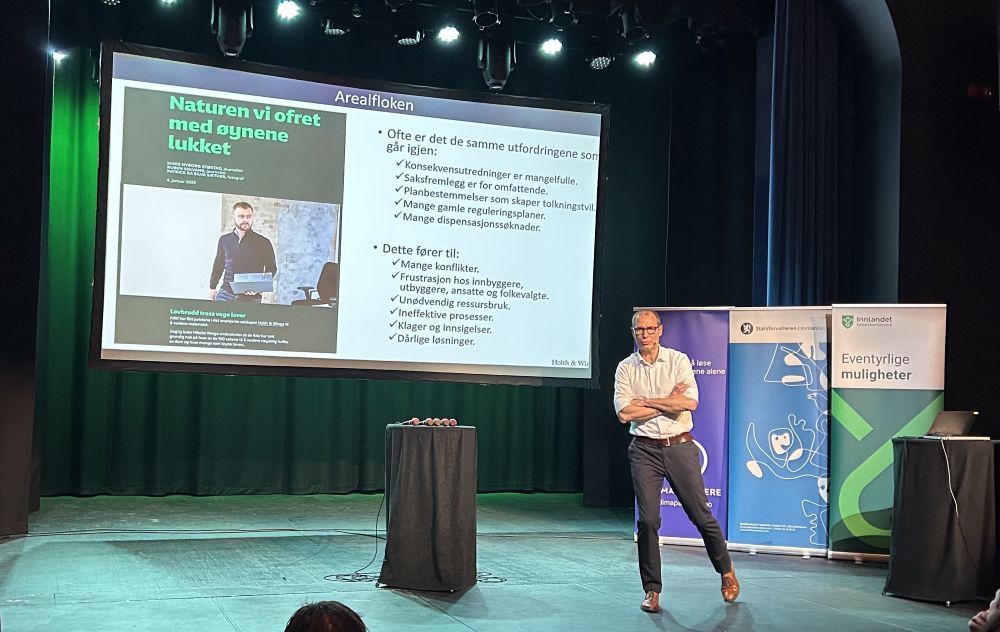 En mann står på en scene forran en presentasjon på et stort lerret