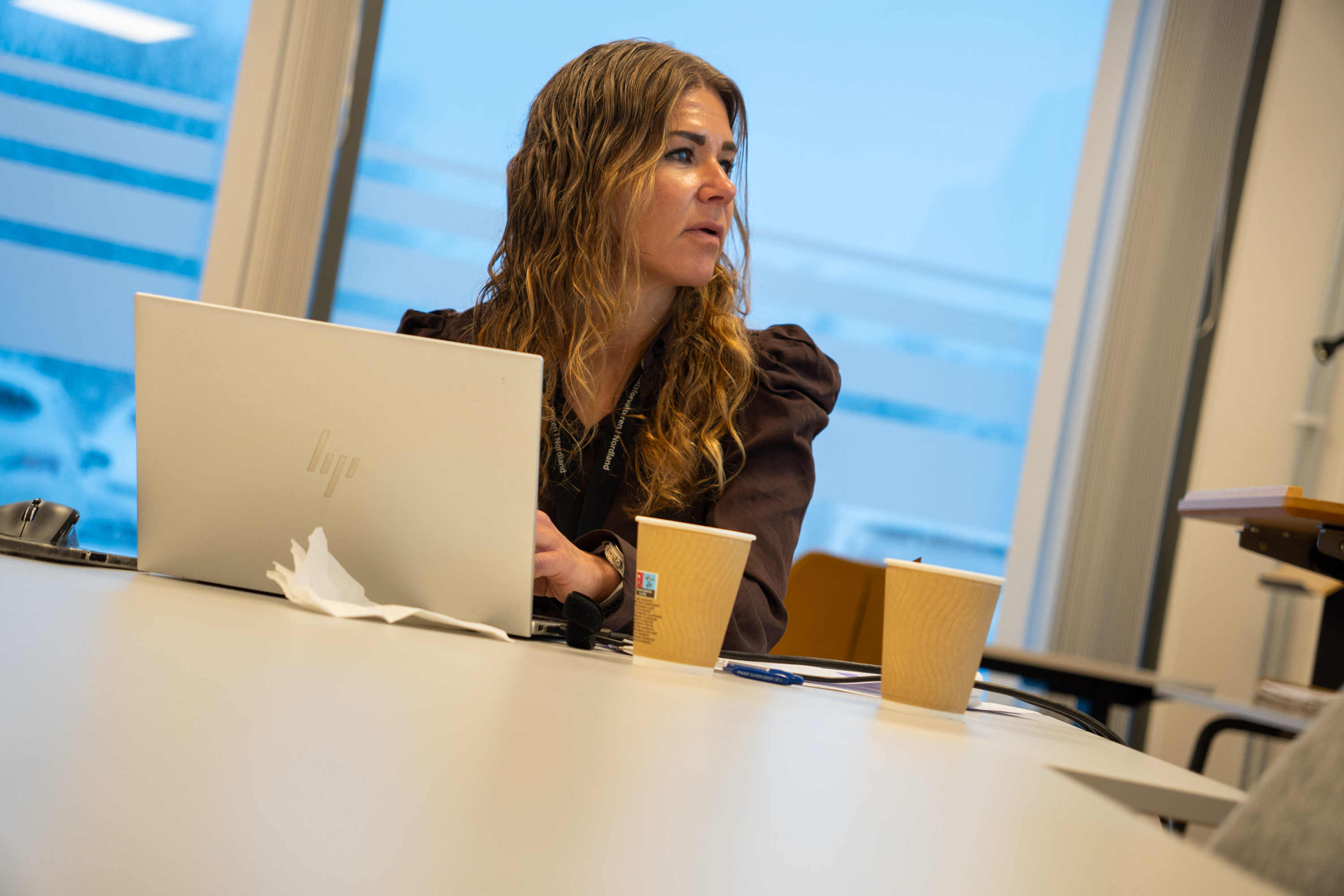 En kvinne sitter ved et bord med en PC og kaffekopper foran seg.