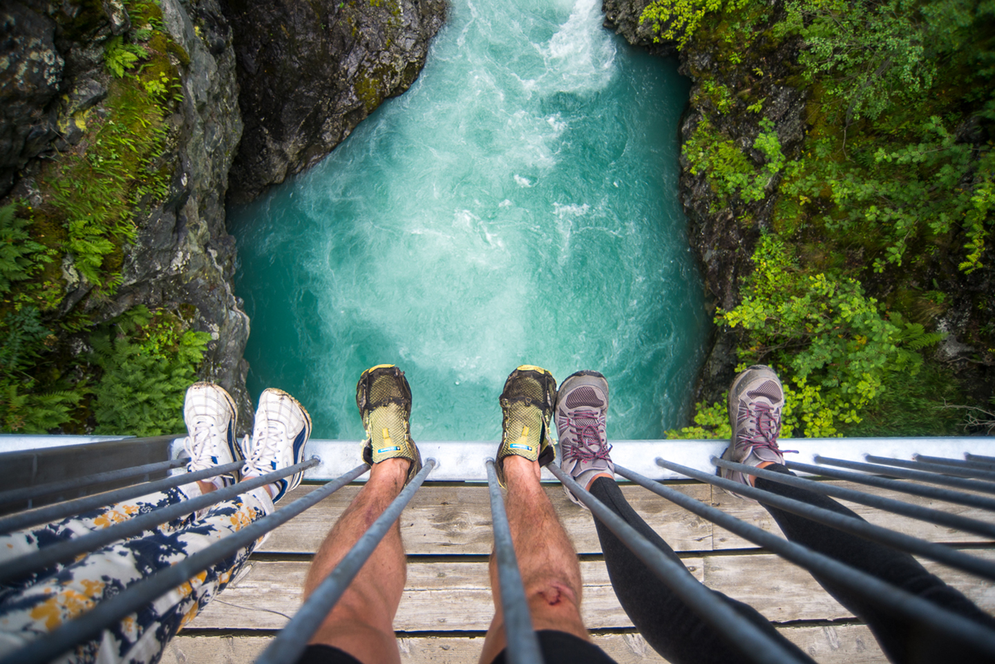 Bilde viser beina til tre personar som står på ei bru over ein foss