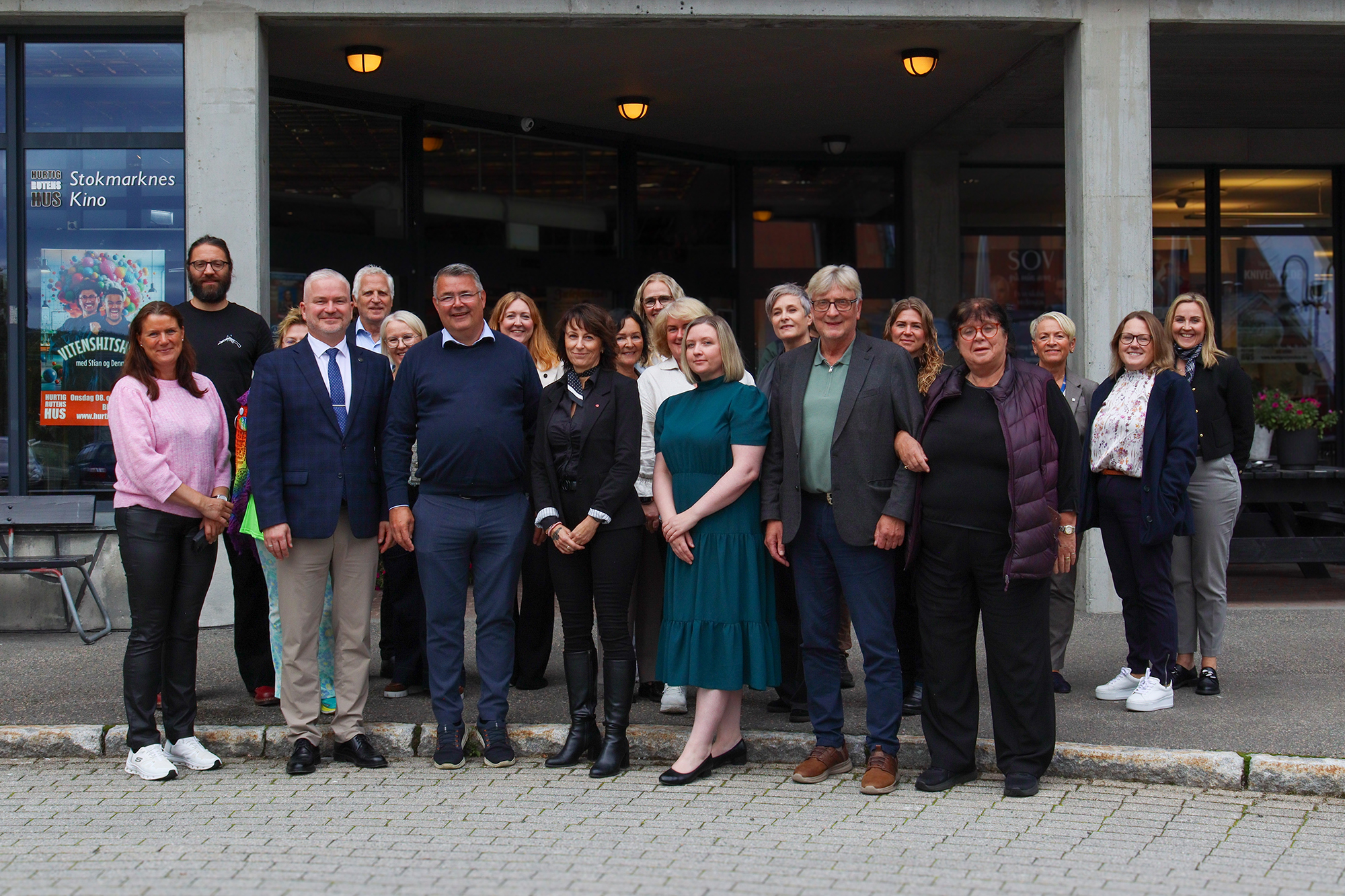 En gruppe mennesker står på fortauet foran inngangen til en stor bygning.