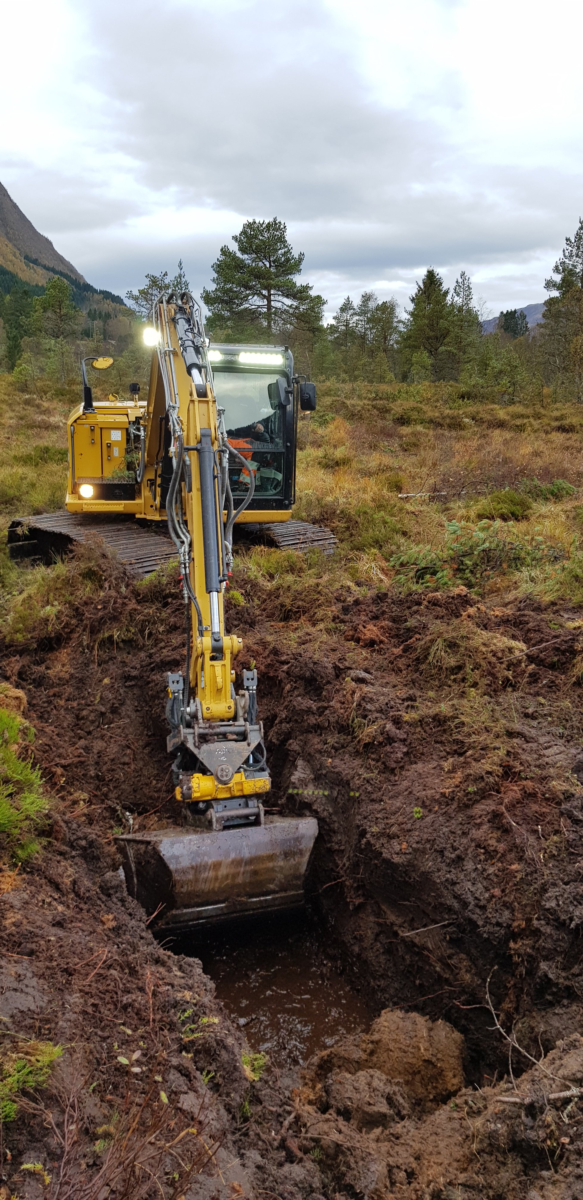 Gravemaskin lagar demning for å avskjære lekkasje av vatn frå høgmyra.