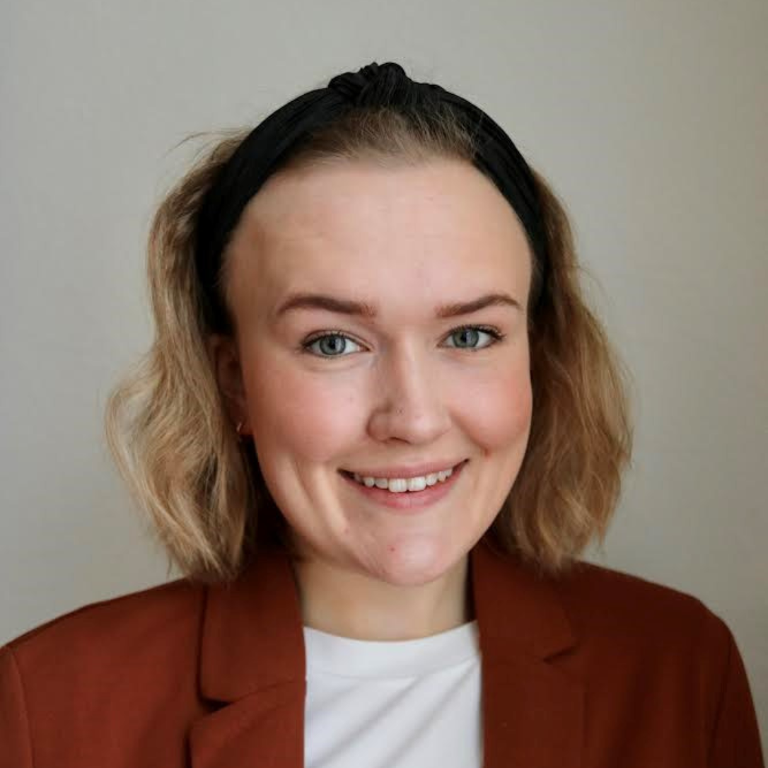 Smilende kvinne med lyst hår, sort hårbånd og rød dressjakke. 