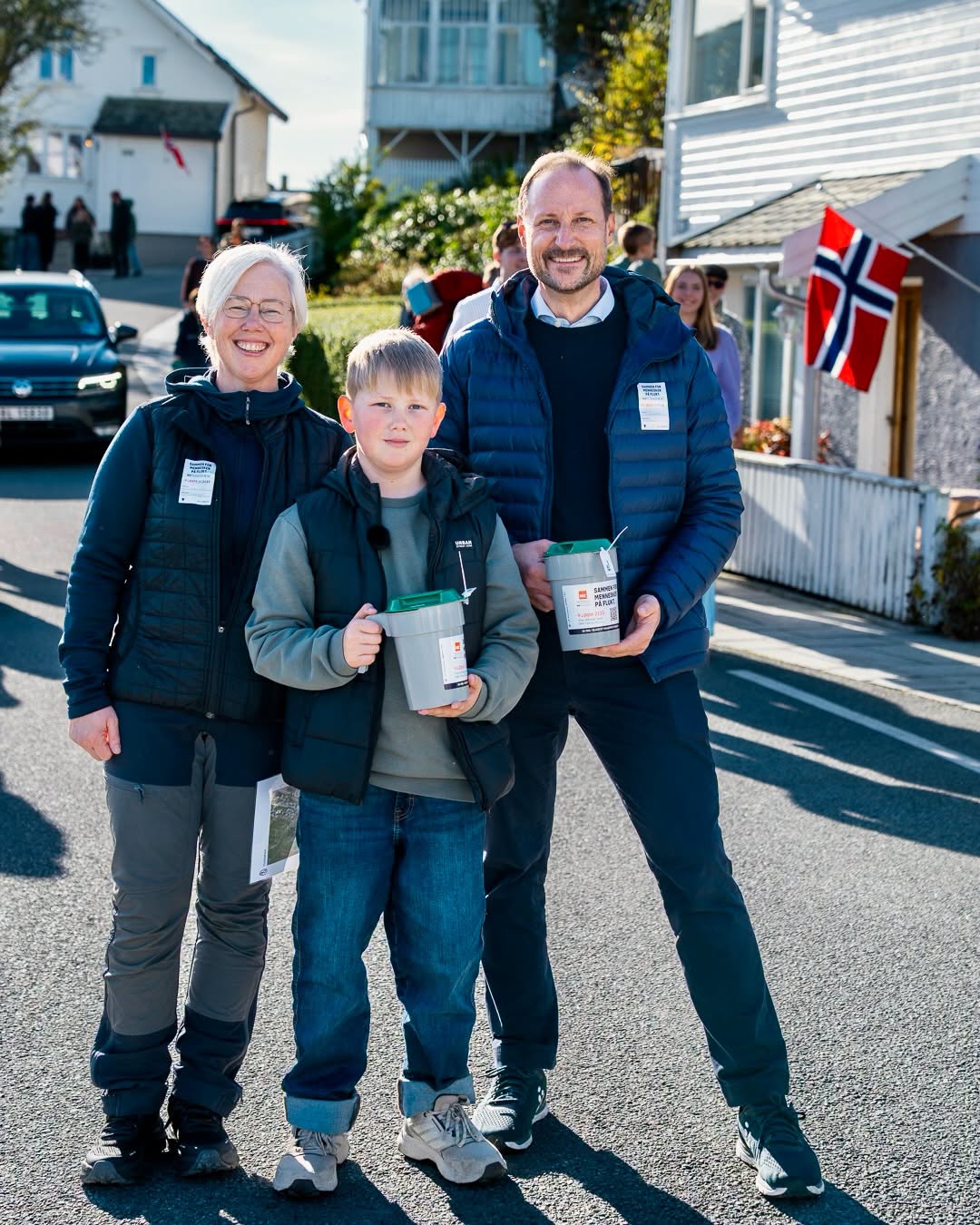Kong Haakon går med innsamlingsbøsse sammen med Camilla og Lasse Lange på Kvitsøy.