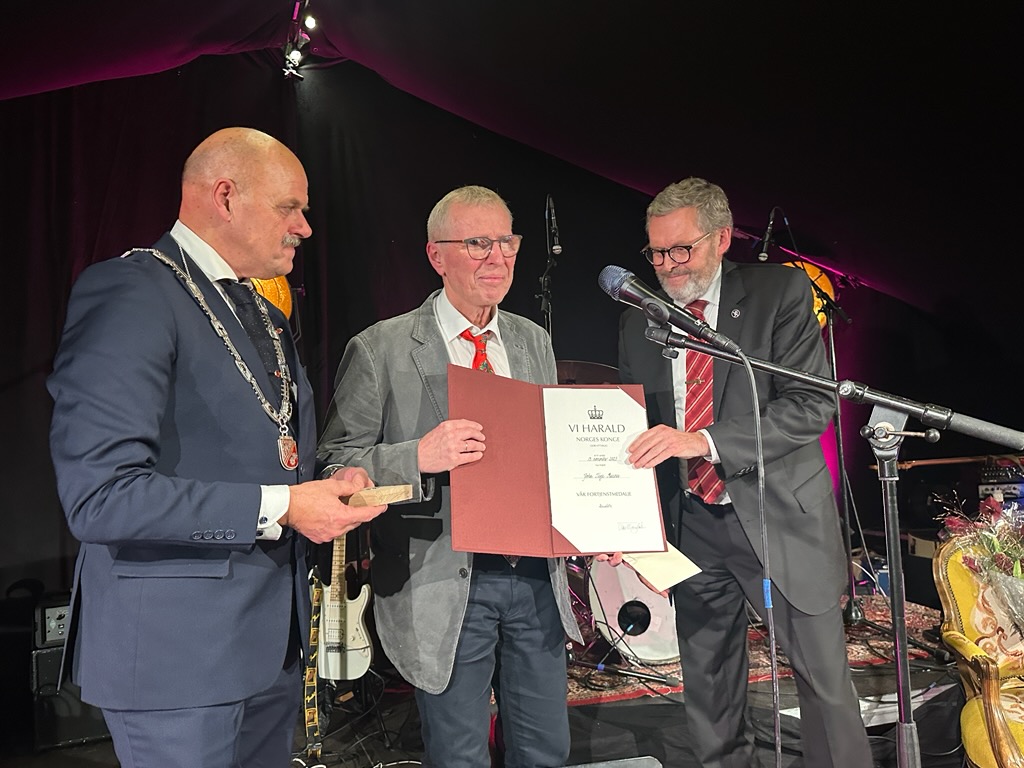 John Terje Ruenes med diplom, stående i midten sammen med ass. statsforvalter Knut Berg og ordfører Nils Olav Larsen. 