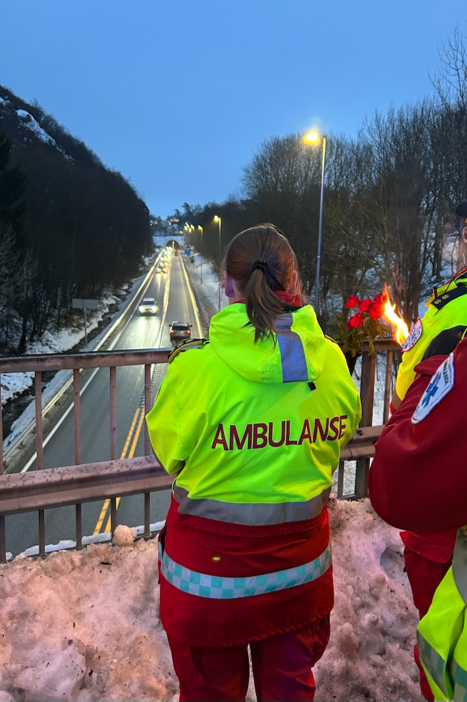 Ambulansepersonell med fakkel ser på trafikken som kjører forbi.