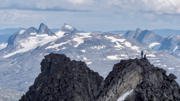 to små menneskje i eit stort fjellandskap med ytsyn over alpine toppar med snø