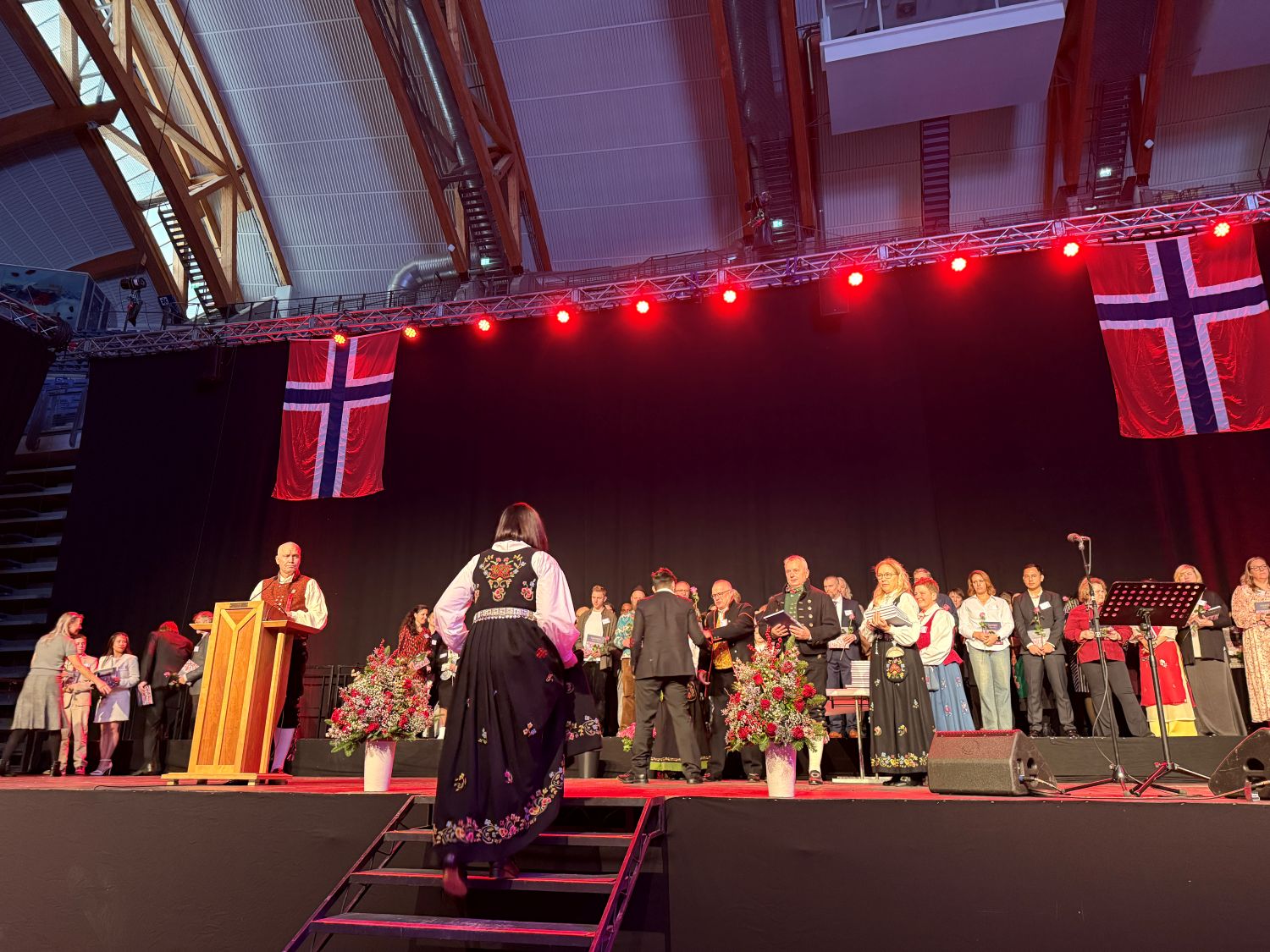 Festkledde mennesker på vei opp på en stor scene der de får utdelt blomster