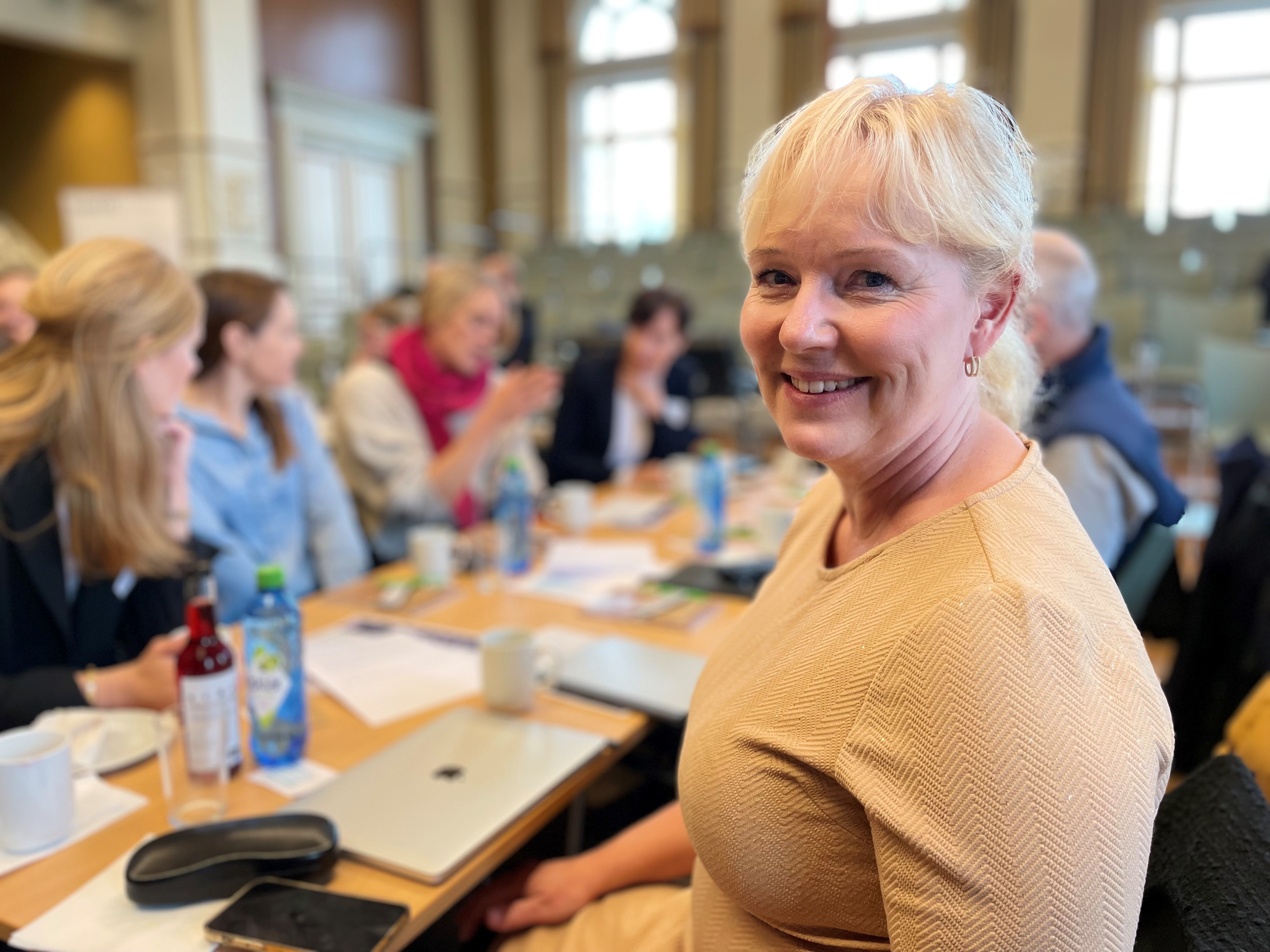 Marte Kvittum Tangen, leder av Norsk forening for allmennmedisin. Foto: Kristina Skamsar. Dame sitter foran en gruppe menneskler som driver med fruppearbneid.