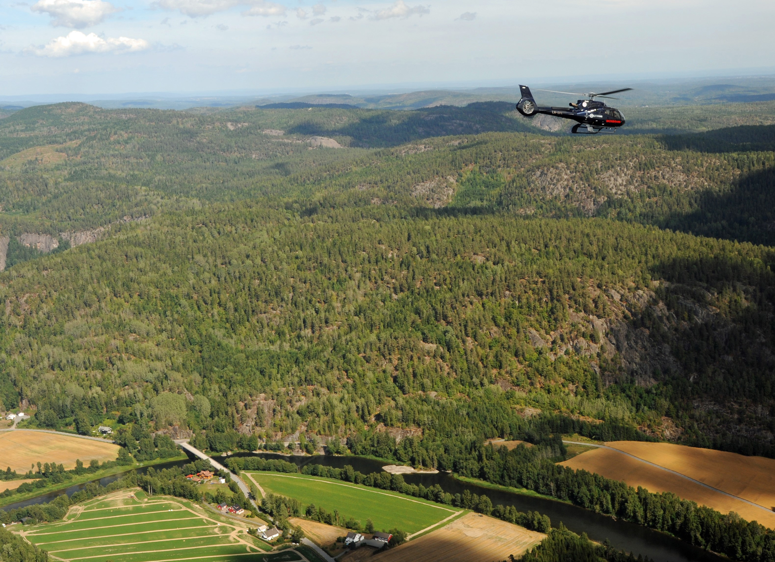 Bildet viser et skogbrannhelikopter som svever over skogen. 